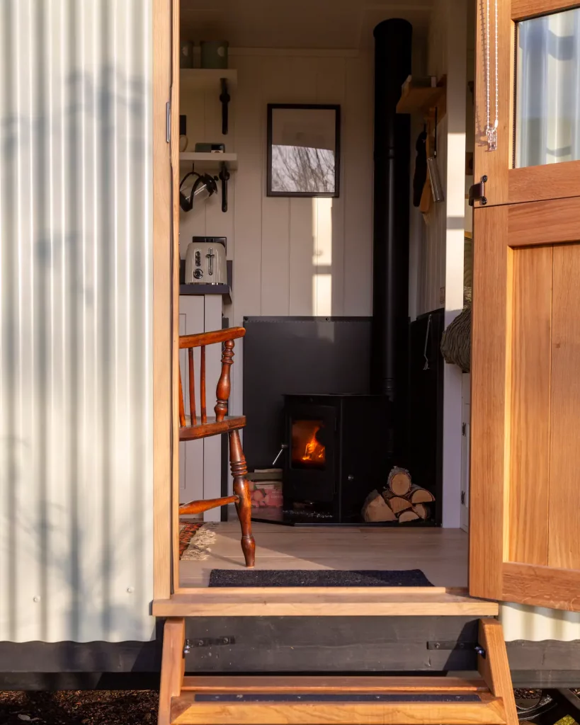 Shepherd's hut door open with a view inside where a wood burning stove is lit